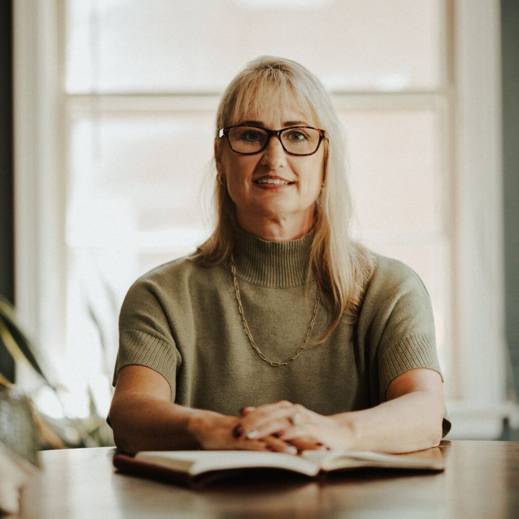 Women in green shirt with long blonde hair sitting at a desk with a journal