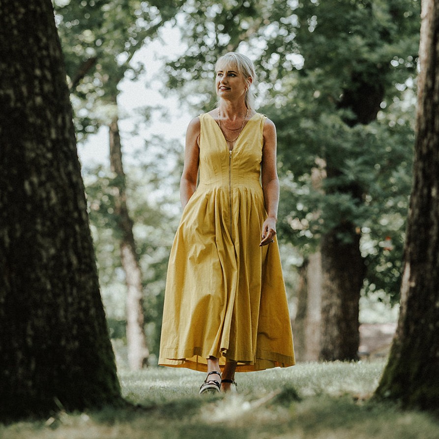 Woman in yellow dress walking in oak grove in summer