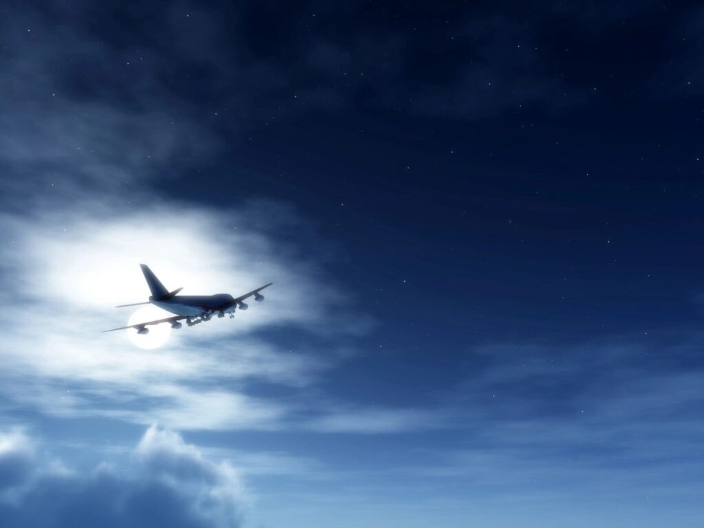 Jet plane flying against a moonlit night.